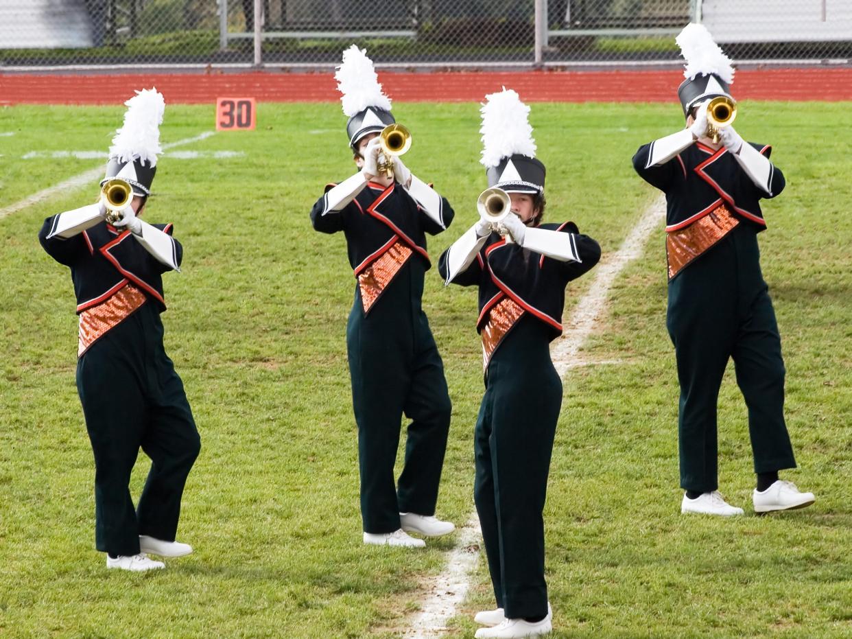 Four brass band players playing on a football pitch.