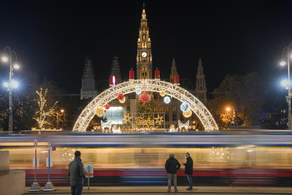 FILE - People wait for the tram, backdropped by the Christmas market, now closed due to the national COVID-19 lockdown, in Vienna, Austria, Nov. 23, 2021. As countries across Europe reimpose lockdowns in response to surging COVID-19 cases and deaths, the UK – long one of Europe’s hardest-hit countries -- carries on with a policy of keeping everything as normal as possible. (AP Photo/Vadim Ghirda, File)