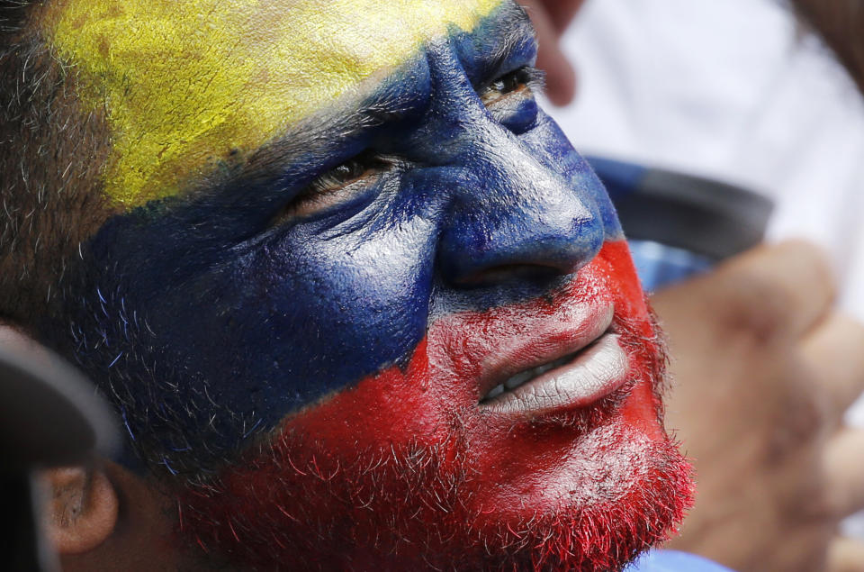 En esta imagen del 12 de febrero de 2019, un hombre con el rostro pintado con los colores de la bandera venezolana, escucha al líder opositor y autoproclamado presidente interino Juan Guaidó durante un mitin en contra del gobierno del mandatario Nicolás Maduro en Caracas. La oposición venezolana convocó a sus simpatizantes a salir a las calles de todo el país en una campaña para despojar del respaldo militar a Maduro, quien se rehúsa a permitir el ingreso de alimentos y medicinas provenientes de Estados Unidos a través de sus fronteras. (AP Foto/Ariana Cubillos)