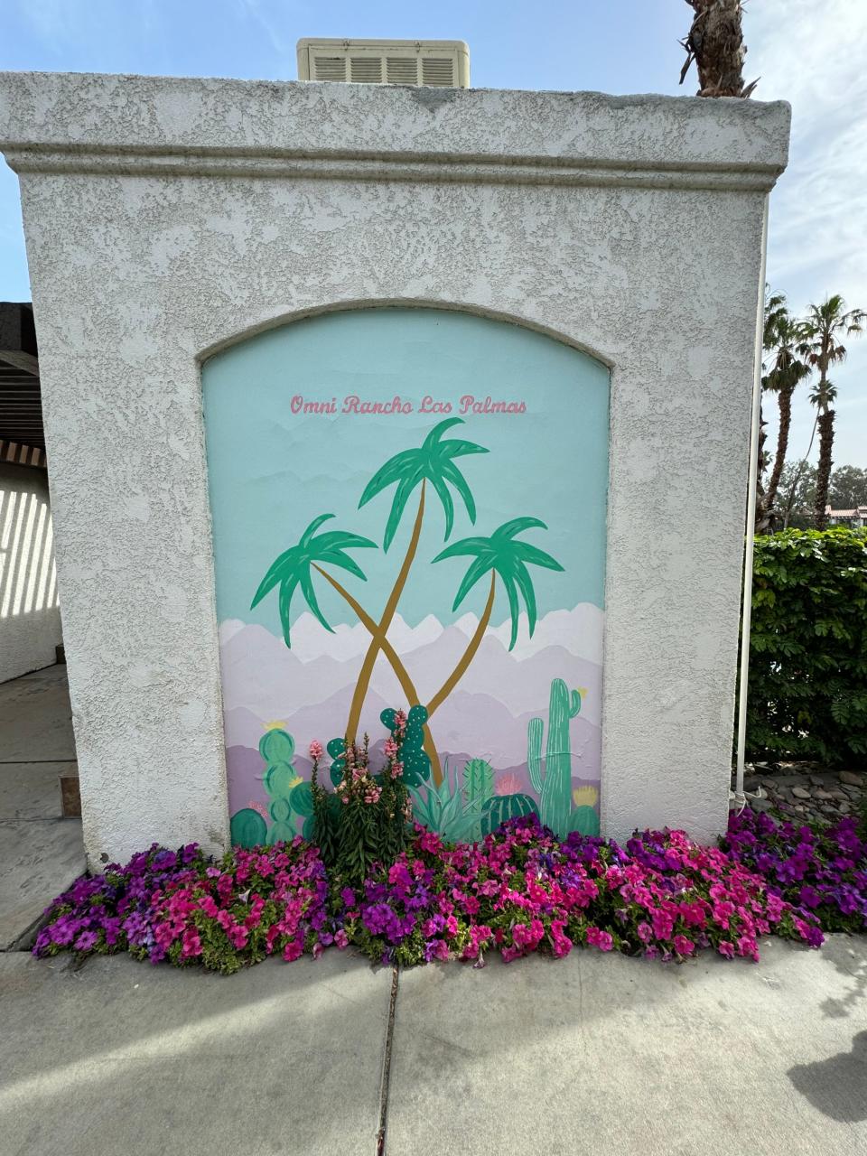 Mural of palm trees and cacti at Omni Rancho Las Palmas, surrounded by vibrant purple flowers