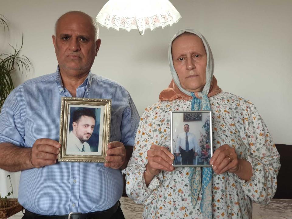 This photo provided by Siyam family, shows Omar Siyam, left, and Siham Siyam, the father and mother of Wassim Siyam who was shot dead by Syrian soldier agents, in the Tadamon neighborhood of Damascus, Syria, hold their son portraits at the their home, in Germany, Wednesday, May 11, 2022. For many years, the Siyam family believed their adult son was being held at a government prison after he went missing at a checkpoint nearly a decade ago. Last month, the hope that he would one day return came to an abrupt end after a newly released video taken in 2013 showed him among dozens of blindfolded young men who were thrown into a large pit and shot dead by Syrian agents, who then set the bodies on fire. (The Family of Wassim Siyam, via AP)