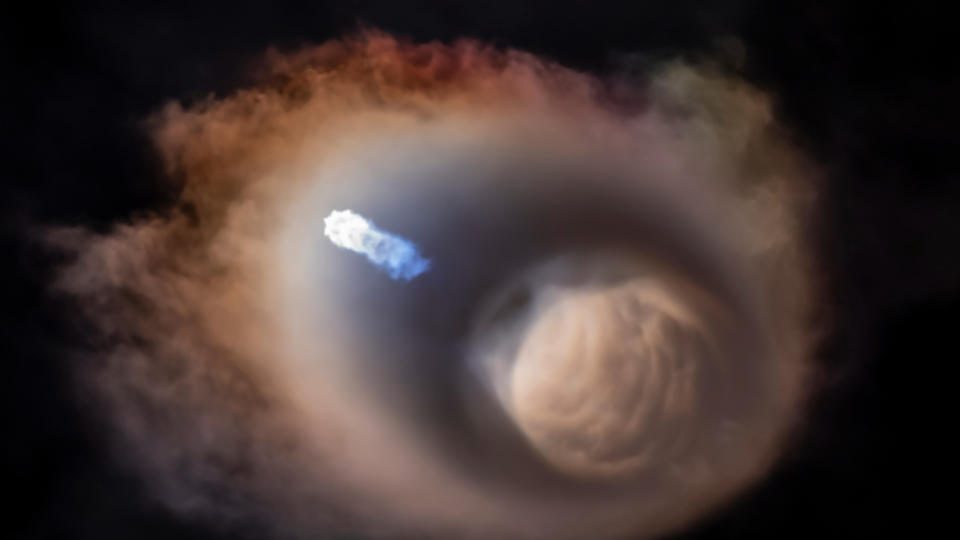 a spacex falcon 9's engines burn bluish-white against a swirling cloud pattern in the night sky.