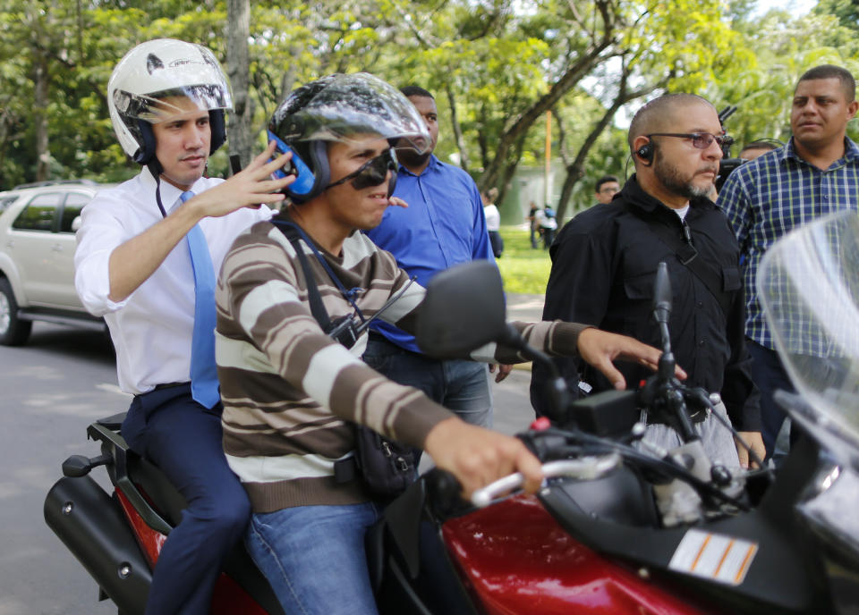 Juan Guaido, Venezuelan opposition leader, and self-proclaimed interim president of Venezuela, adjusts the helmet on a motorcycle driver as he is driven from the Central University of Venezuela after a meeting with students, in Caracas, Venezuela, Thursday, Nov. 14, 2019. (AP Photo/Ariana Cubillos)