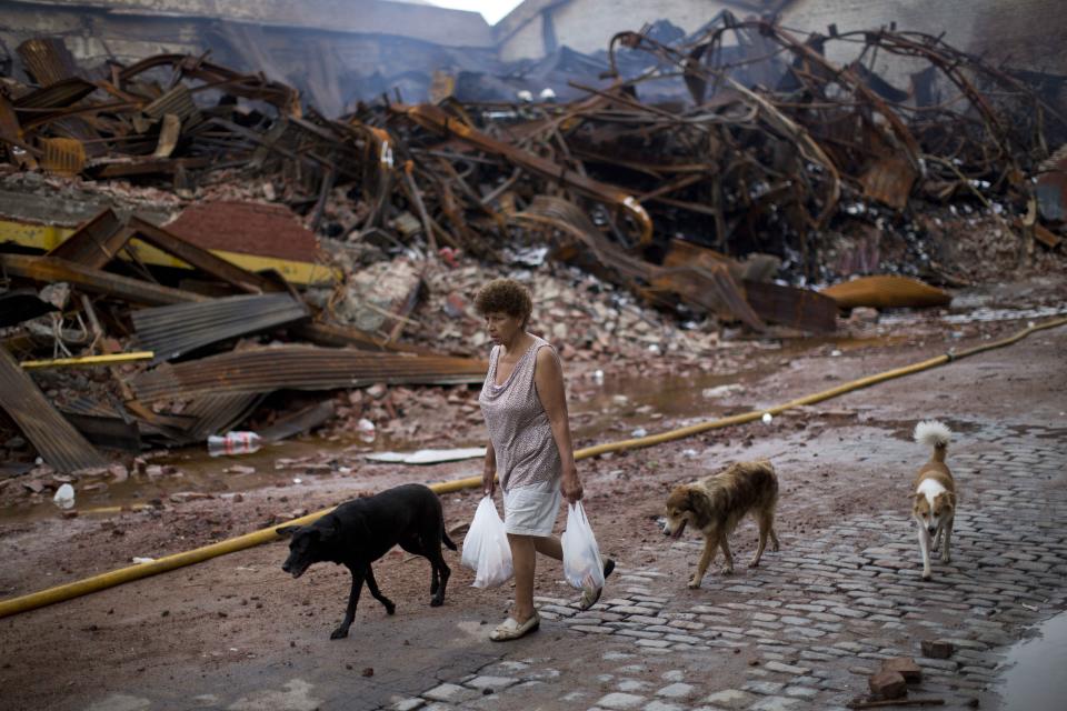 In this Feb. 10, 2014 photo, accompanied by her three dogs, a woman hauls her bags of groceries past the scorched Iron Mountain warehouse in Buenos Aires, Argentina. Argentines have suffered through a tough summer, with tropical rain that provided no relief from the heat and humidity, people having to throw out rotten food because of rolling power blackouts and soaring oil and gas prices, all amid rising inflation that is making it ever harder to reach the end of the month. The strain is evident on the faces of subway riders and others making their way home in Buenos Aires, where signs of poverty and decay are ubiquitous just beyond the glamorous streets where tourists go. (AP Photo/Rodrigo Abd)