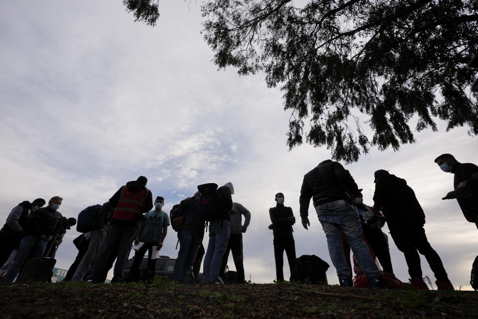 Migrants stand in groups as they arrive at a bus stop after leaving a processing facility, Friday, Feb. 23, 2024, in San Diego. Hundreds of migrants were dropped off Friday at a sidewalk bus stop amid office parks in San Diego with notices to appear in immigration court after local government funding for a reception center ran out of money sooner than expected. (AP Photo/Gregory Bull)