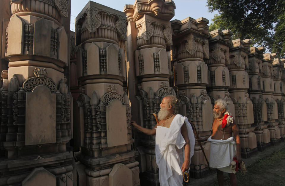 FILE - In this Friday, Oct. 1, 2010, file photo, Hindu holy men look at pillars lying at a workshop for the construction of a Rama temple in Ayodhya, India. State-run broadcaster says India’s top court has ruled for a disputed temple-mosque land for Hindus with alternate land to Muslims. The Supreme Court says in a judgment on Saturday, Nov. 9, 2019, that 5 acres (2.02 hecatres) of land be allotted to the Muslim community represented by the Sunni Central Wakf Board in the northern Indian town of Ayodhya where a 16th century mosque was demolished by Hindu hardliners in 1992. (AP Photo/Rajesh Kumar Singh, File)