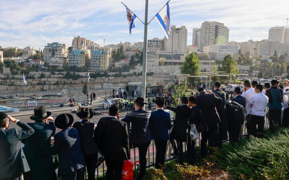 Ultra-Orthodox Jews look on as police and security forces secure the site of a shooting in Jerusalem