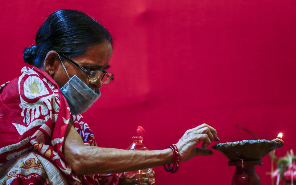 An elderly Indian woman wearing a face mask lights an oil lamp inside a makeshift worship venue during Durga Puja, the biggest festival of the region, in Kolkata, India, Sunday, Oct. 25, 2020. The Hindu festival season is traditionally laced with an unmatched fanfare and extravaganza, with socializing being the hallmark of the celebration. But because of the coronavirus pandemic this year's festivities have started on a pale note. (AP Photo/Bikas Das)