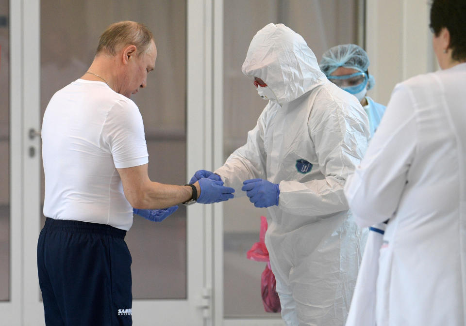 Russian President Vladimir Putin, left, dons gloves during his visit to the hospital for coronavirus patients in Kommunarka settlement, outside Moscow, Russia, Tuesday, March 24, 2020. Putin praised its doctors for high professionalism, saying they were working "like clockwork." For some people the COVID-19 coronavirus causes mild or moderate symptoms, but for some it can cause severe illness including pneumonia.(Alexei Druzhinin, Sputnik, Kremlin Pool Photo via AP)