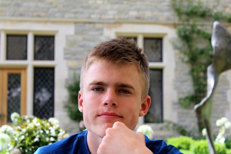 A picture of a young man taken outside, with a building in the background.