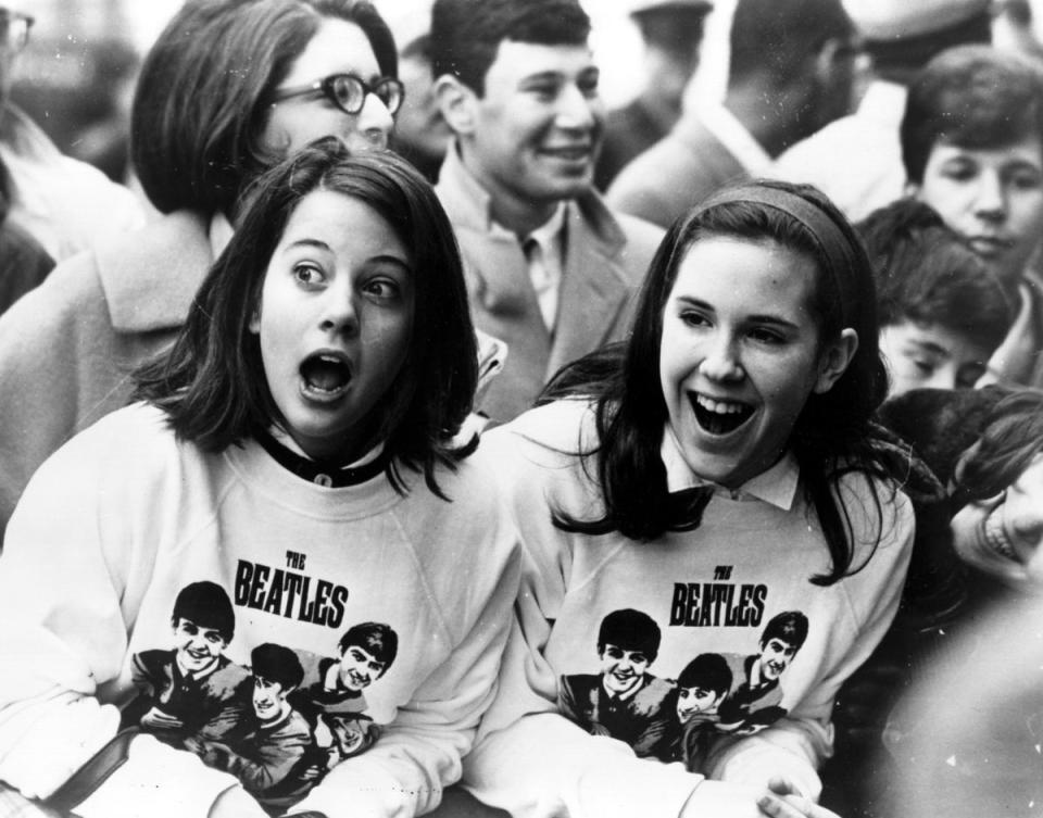 Two excited girls in Beatles sweatshirts among a crowd of fans in New York, welcoming the group as they arrive at the airport in February 1964 (Getty)