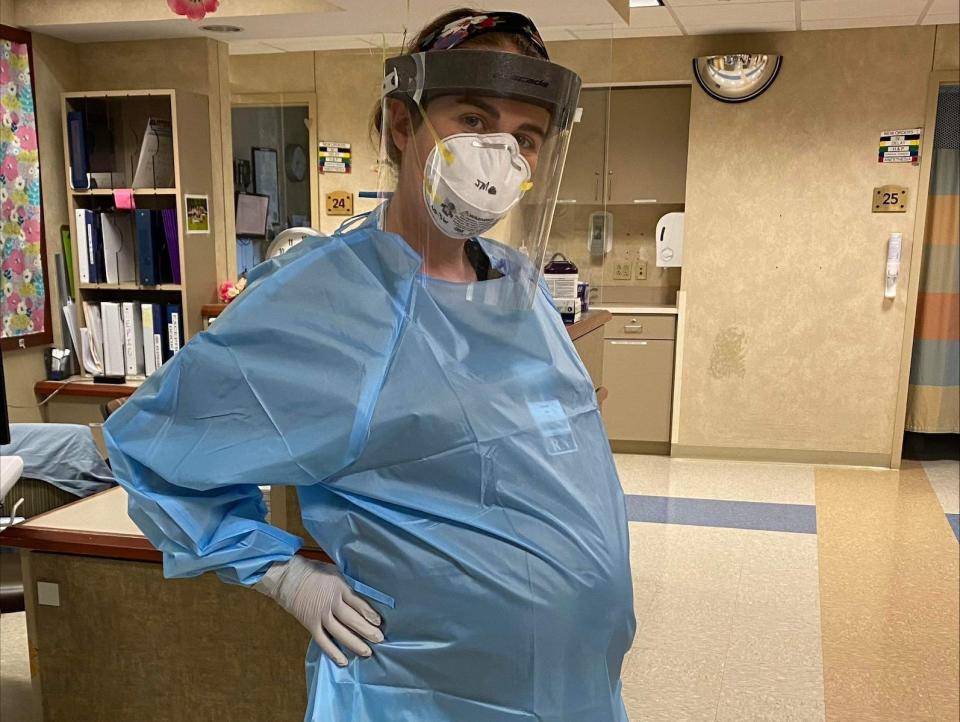 Jenny Miles, who is 8 months pregnant, poses in her hospital unit wearing scrubs.