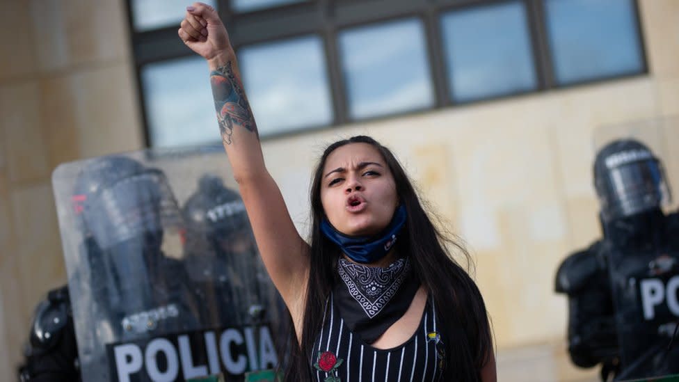 Mujer con el brazo levantado. Detrás la policía