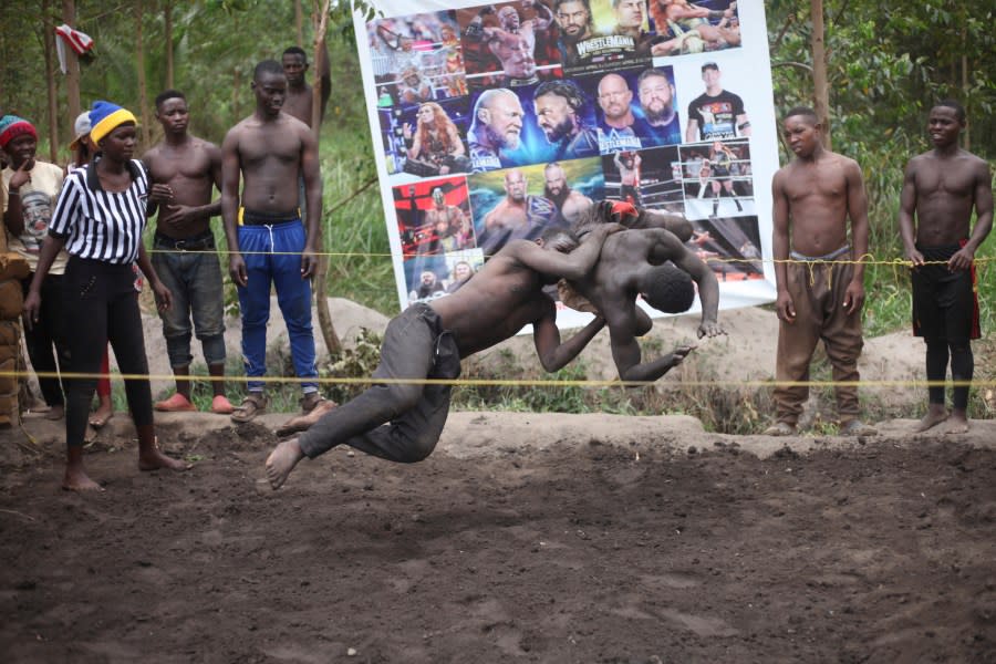 Ugandan youths perform an amateur wrestling tangle in the soft mud in Kampala, Uganda Wednesday, March. 20, 2023. The open-air training sessions, complete with an announcer and a referee, imitate the pro wrestling contests the youth regularly see on television. While a pair tangles inside the ring, made with bamboo poles strung with sisal rope, others standing ringside cheer feints and muscular shows of strength. (AP Photo/Patrick Onen)