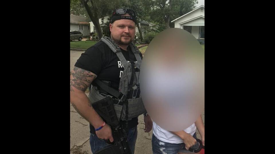 Michael Eckerman, holding an assault rifle and wearing a tactical vest, stands next to his wife.