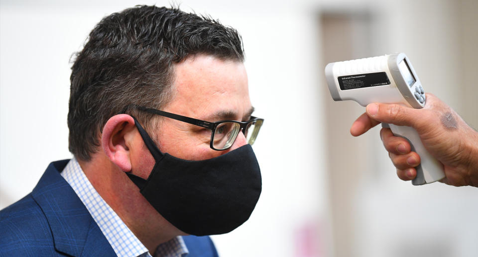 Daniel Andrews getting his temperature checked while wearing a mask.