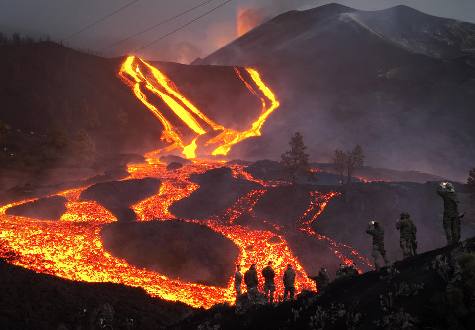 FILE - Spanish Army soldiers stand on a hill as lava flows as volcano continues to erupt on the Canary island of La Palma, Spain, on Nov. 29, 2021. Authorities on a Spanish island are declaring a volcanic eruption that has caused widespread damage but no casualties officially finished, following ten days of no significant sulfur dioxide emissions, lava flows or seismic activity. But the emergency in La Palma, the northwesternmost of the Atlantic Ocean's Canary Islands, is not over yet, said the director of the archipelago’s volcanic emergency committee, or Pevolca, Julio Pérez. (AP Photo/Emilio Morenatti, File)