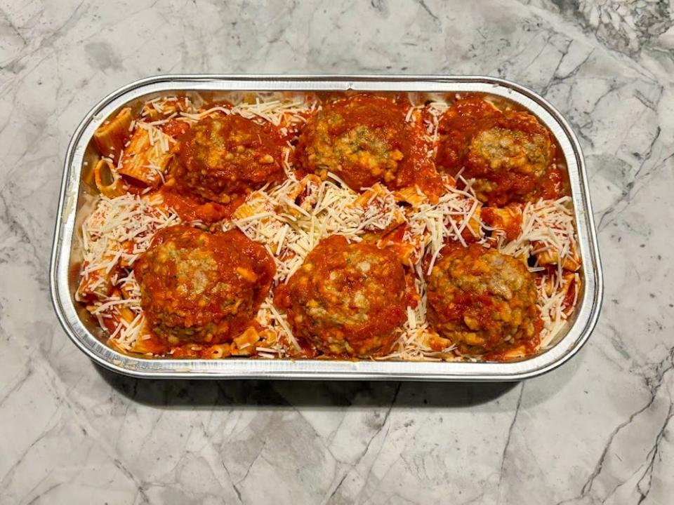 A silver tray of rigatoni pasta and six large meatballs, with a red sauce and cheese covering the pasta