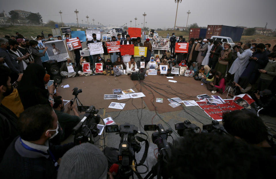Nasrullah Baluch, center bottom, leader of the Voice of Baluch Missing Persons, speaks while people hold placards and portraits of their missing family members during a press conference in Islamabad, Pakistan, Saturday, Feb. 20, 2021. Dozens of relatives of Baluch missing persons, allegedly taken away by security agencies from restive Baluchistan province, Saturday ended their ten-day protest sleeping in the February cold near Pakistan parliament in capital Islamabad as minster for Human Rights assured their demand for recovery of loved ones would be taken seriously. (AP Photo/Anjum Naveed)