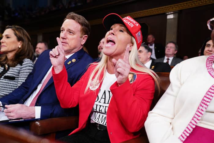 MTG in a "Make America Great Again" hat gesturing, seated next to a man in a suit at the SOTU
