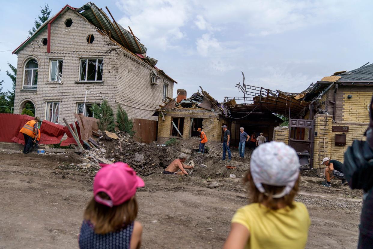 Children watch as workers clean up after a rocket strike on a house in Kramatorsk, Donetsk region, eastern Ukraine, Friday, Aug. 12, 2022. 