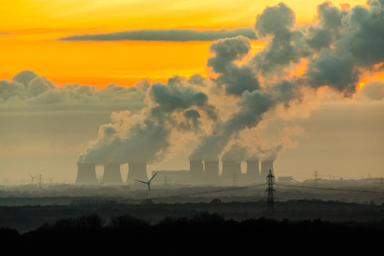 The imposing cooling towers of a power station near the village of Drax in North Yorkshire.  Plumes of water vapor leave a trail in the cold November night air.   Horizontal.  Space for copy.