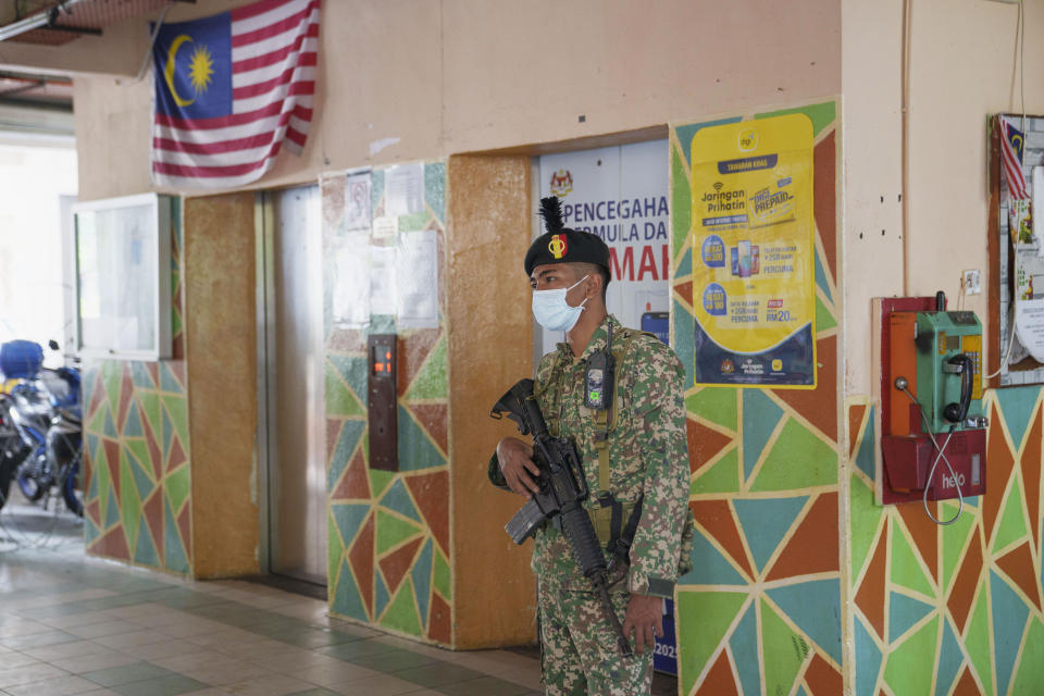 An armed soldier stands guard at the entrance of a high density residential area placed under the enhanced movement control order (EMCO) due to drastic increase in the number of COVID-19 cases recorded at Sentul in Kuala Lumpur, Malaysia, Saturday, July 3, 2021. Malaysia starts further tighten movement curbs and imposes a curfew in most areas in its richest state Selangor and parts of Kuala Lumpur, where coronavirus cases remain high despite a national lockdown last month. (AP Photo/Vincent Thian)