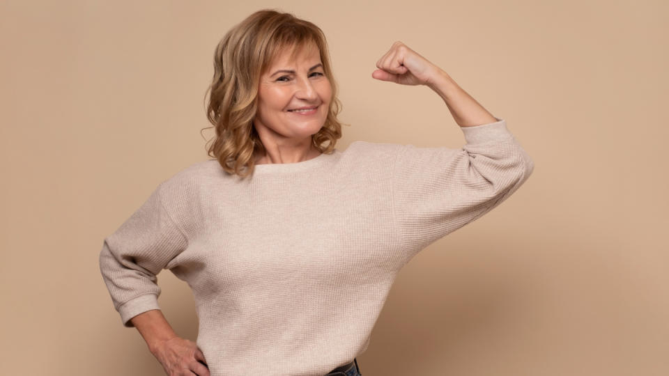 A woman with short hair and a tan sweat flexing her bicep 