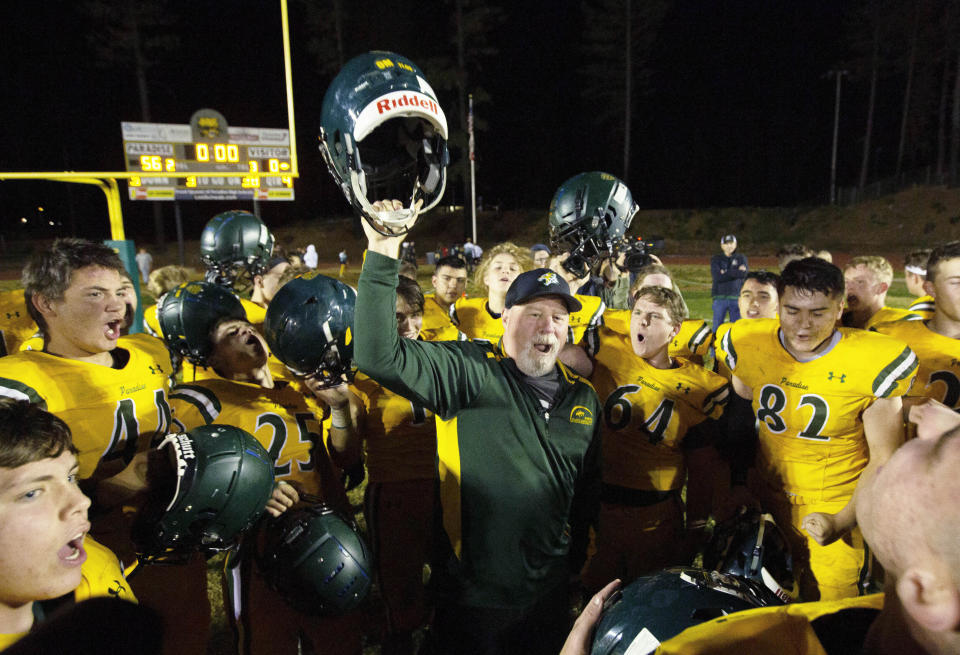 FILE - In this Nov. 15, 2019 file photo, Paradise High School head football coach Rick Prinz, center, celebrates with his team after defeating Live Oak High School in their Northern California Division III playoff game in Paradise, Calif. Paradise, the Northern California high school football team is preparing to play for a championship one year after most of the players and coaches lost their homes to a wildfire that nearly destroyed their town. Paradise High School will face Sutter Union High School on Saturday, Nov. 30 for the Northern Section Division III championship.(AP Photo/Rich Pedroncelli, File)