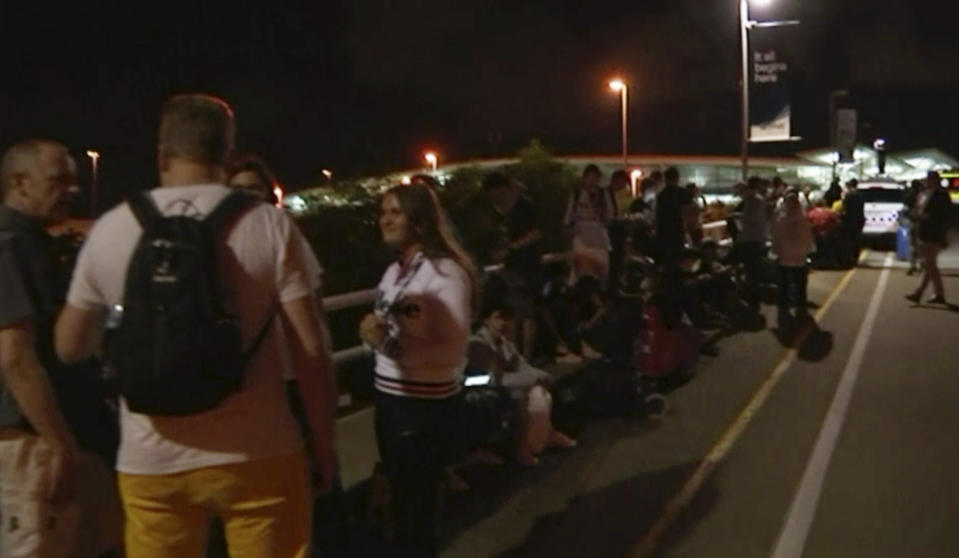 In this image made from a video taken on Saturday, Feb. 2, 2019, travelers stay outside Brisbane International Airport after their evacuation from the airport in Brisbane, Australia. A man who falsely claimed to have a bomb and menaced a woman with a knife forced the evacuation of Brisbane International Airport for more than two hours, police said on Sunday. (Australian Broadcasting Corporation via AP)