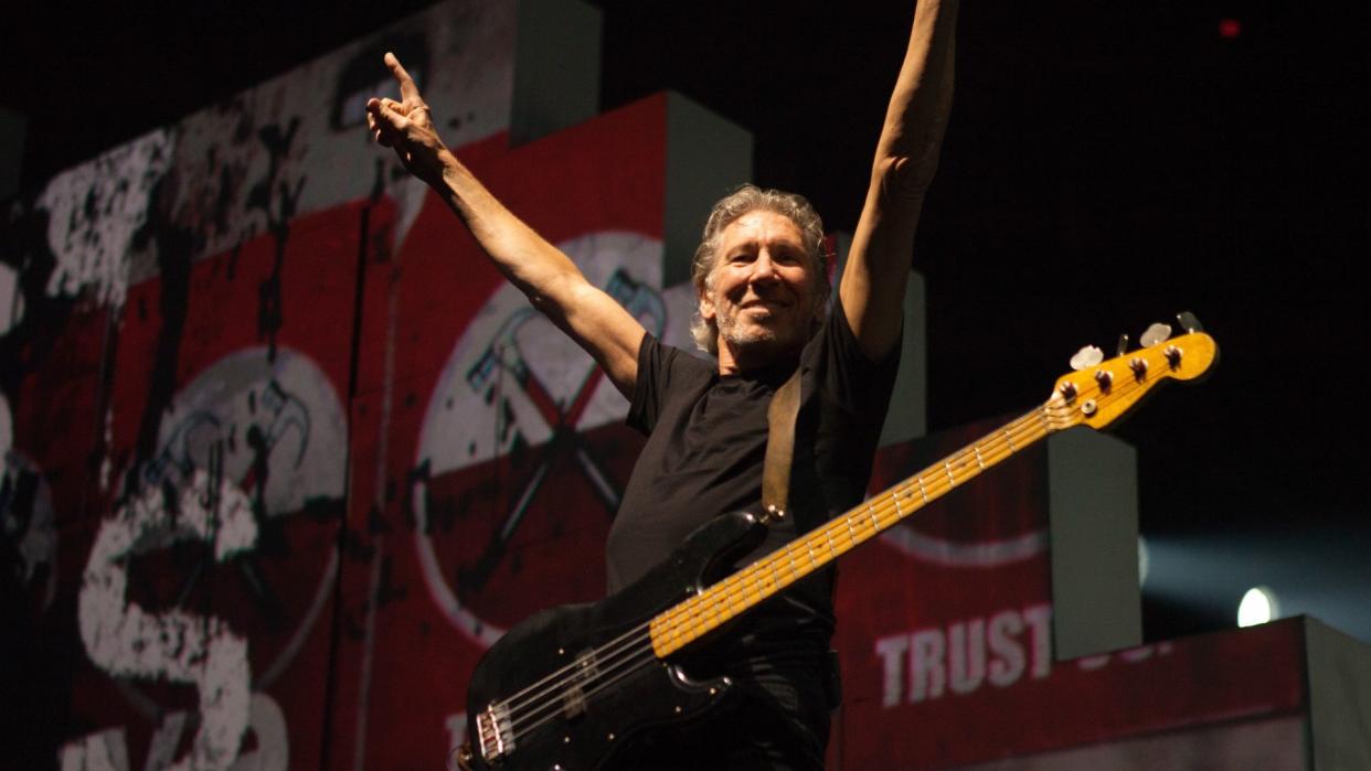  photo of Pink Floyd bass player Roger Waters  raising his arms above his head and smiling from the stage at a concert in 2012 