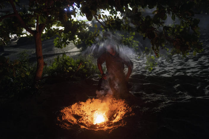 Minutes before midnight, Pastor Cleiton Pereira kneels before a fire pit as he burns scrawled prayers on scraps of paper in an area of the Abaete dune system evangelicals have come to call the "Holy Mountain", in Salvador, Brazil, late Friday night, Sept. 16, 2022. Evangelicals have been converging on the dunes for some 25 years but especially lately, with thousands now coming each week to sing, pray and enter trancelike states to commune with God.(AP Photo/Rodrigo Abd)