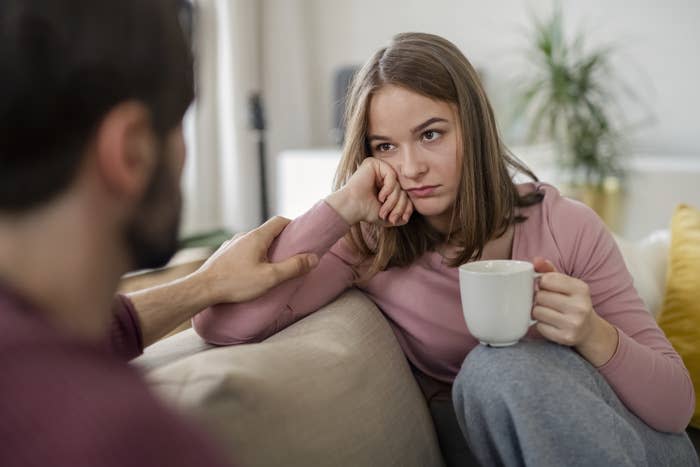 A girl looking sad sitting with a white mug on a couch facing a man