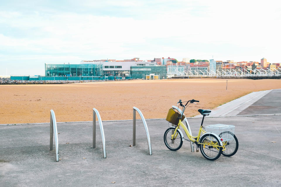 Bicycle parked near an empty bike rack with a beach and buildings in the background on a clear day