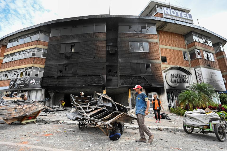 People take out scrap metal from hotel burned last night during clashes between demonstrators and riot police officers in the protests against the government's tax reform in Cali. / Credit: LUIS ROBAYO/AFP via Getty Images