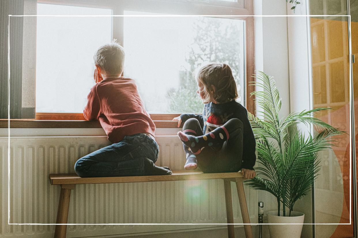  Young children sat on bench by radiator looking out of the window. 