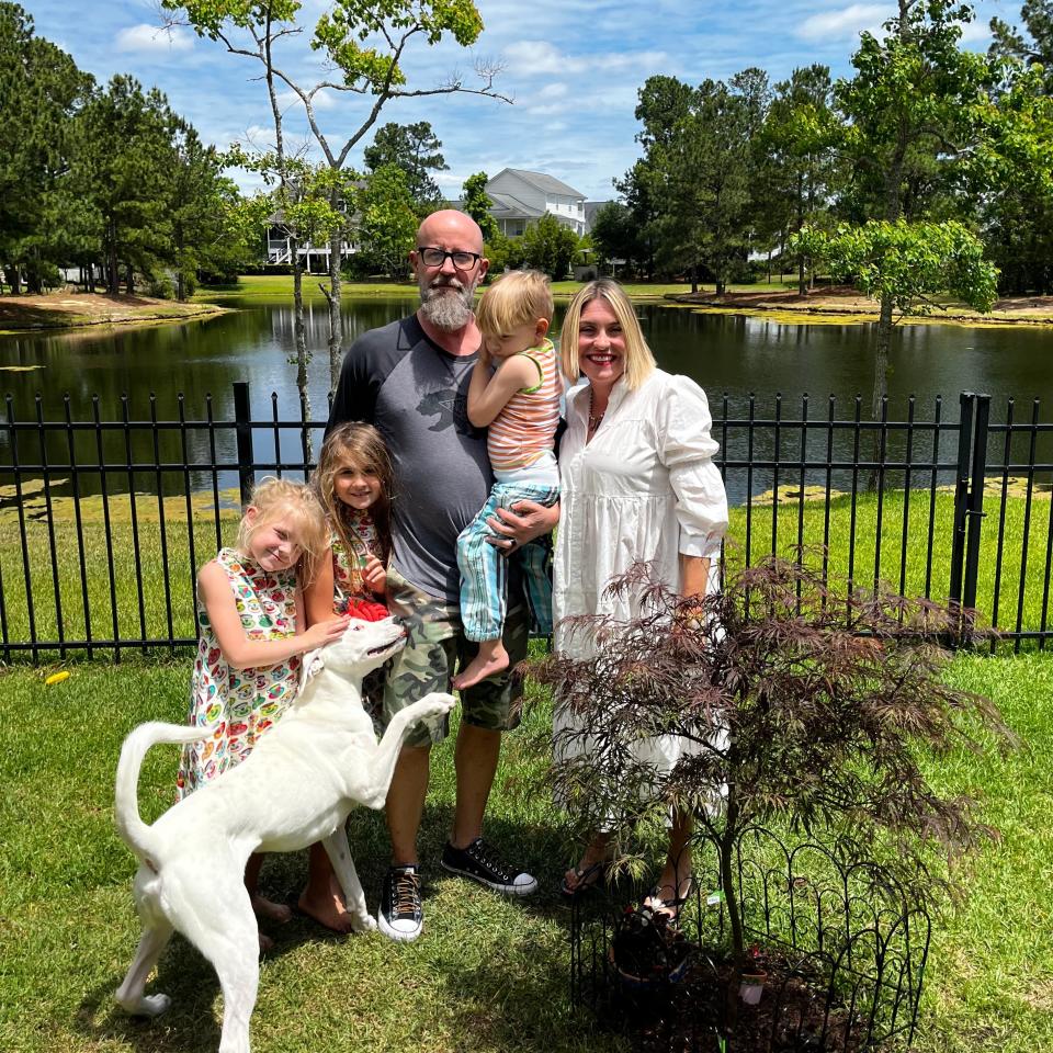 May Lane Hart stands in her backyard with her husband, three kids, and dog.