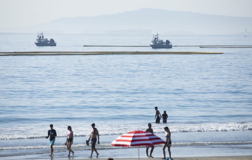 HUNTINGTON BEACH, CA - OCTOBER 03: Beachgoers at Newport Beach enjoy the afternoon as boats drag oil booms offshore on Sunday, Oct. 3, 2021. Authorities said 126,000 gallons of oil leaked from the offshore oil rig Elly on Saturday affecting Huntington Beach and Newport Beach. (Myung J. Chun / Los Angeles Times)