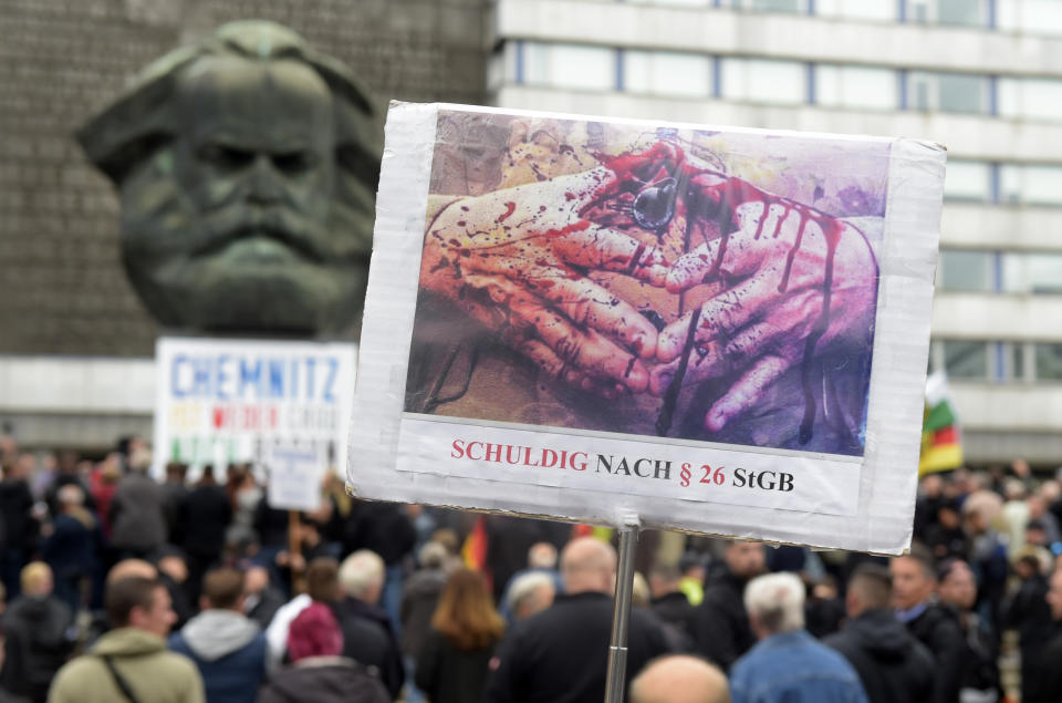 A protestor holds a poster with a photo of Angela Merkel's trademark gesture referring reading she is guilty of incitement in Chemnitz, eastern Germany, Saturday, Sept. 1, 2018, after several nationalist groups called for marches protesting the killing of a German man last week, allegedly by migrants from Syria and Iraq. (AP Photo/Jens Meyer)