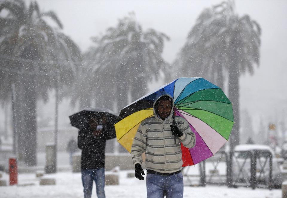 Men holding umbrellas walk outside Jerusalem's Old City during snowfall December 12, 2013. Snow fell in Jerusalem and parts of the occupied West Bank where schools and offices were widely closed and public transport was paused. REUTERS/Darren Whiteside (JERUSALEM - Tags: ENVIRONMENT)