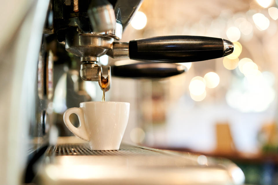 Close-up of industrial coffee maker dripping coffee into a espresso cup, blurry background