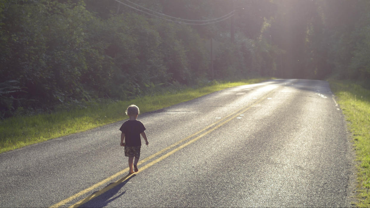 A boy walking alone down an empty road