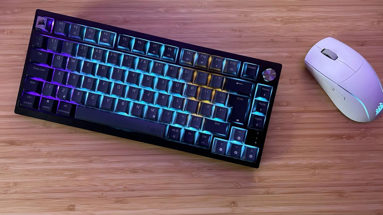  Corsair K65 Plus Wireless with gaming mouse on a wooden desk. 