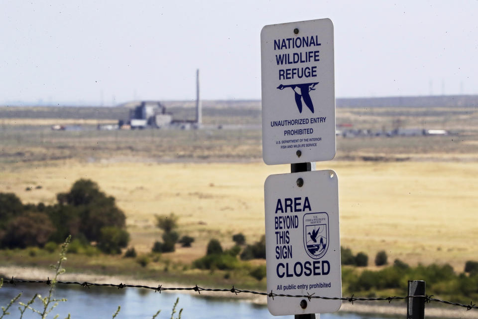 In this Wednesday, Aug. 14, 2019 photo, a sign designates a boundary of the Hanford Reach National Monument as the world's first large scale nuclear reactor, the B Reactor, is seen in the background where it sits unused on the Hanford Nuclear Reservation along the Columbia River near Richland, Wash. The Energy Department estimates it will cost between $323 billion and $677 billion more to finish the costliest cleanup, at the Hanford Site in Washington state where the government produced plutonium for bombs and missiles. (AP Photo/Elaine Thompson)