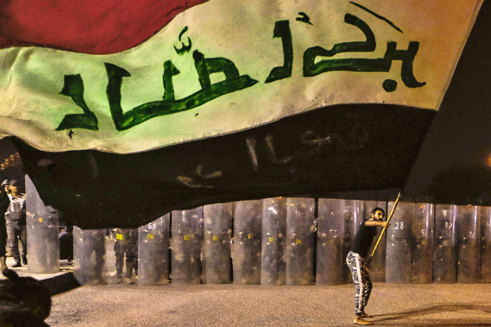 A protester waves an Iraqi flag while Security forces surround the protest site during ongoing anti-government protests in Basra, Iraq, Wednesday, Nov. 4, 2020. (AP Photo/Nabil al-Jurani)