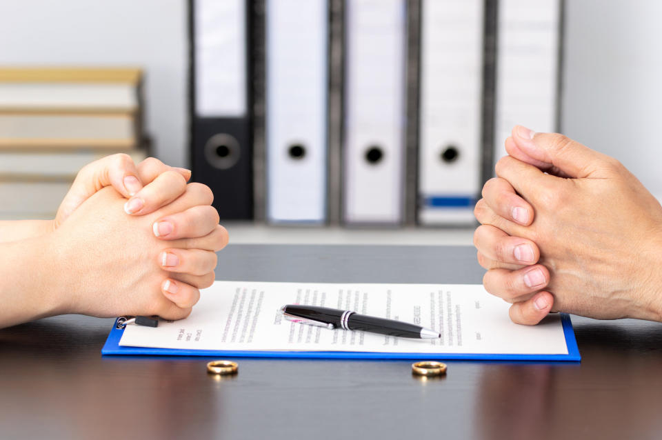 Two pairs of hands placed on divorce papers with wedding bands on the table