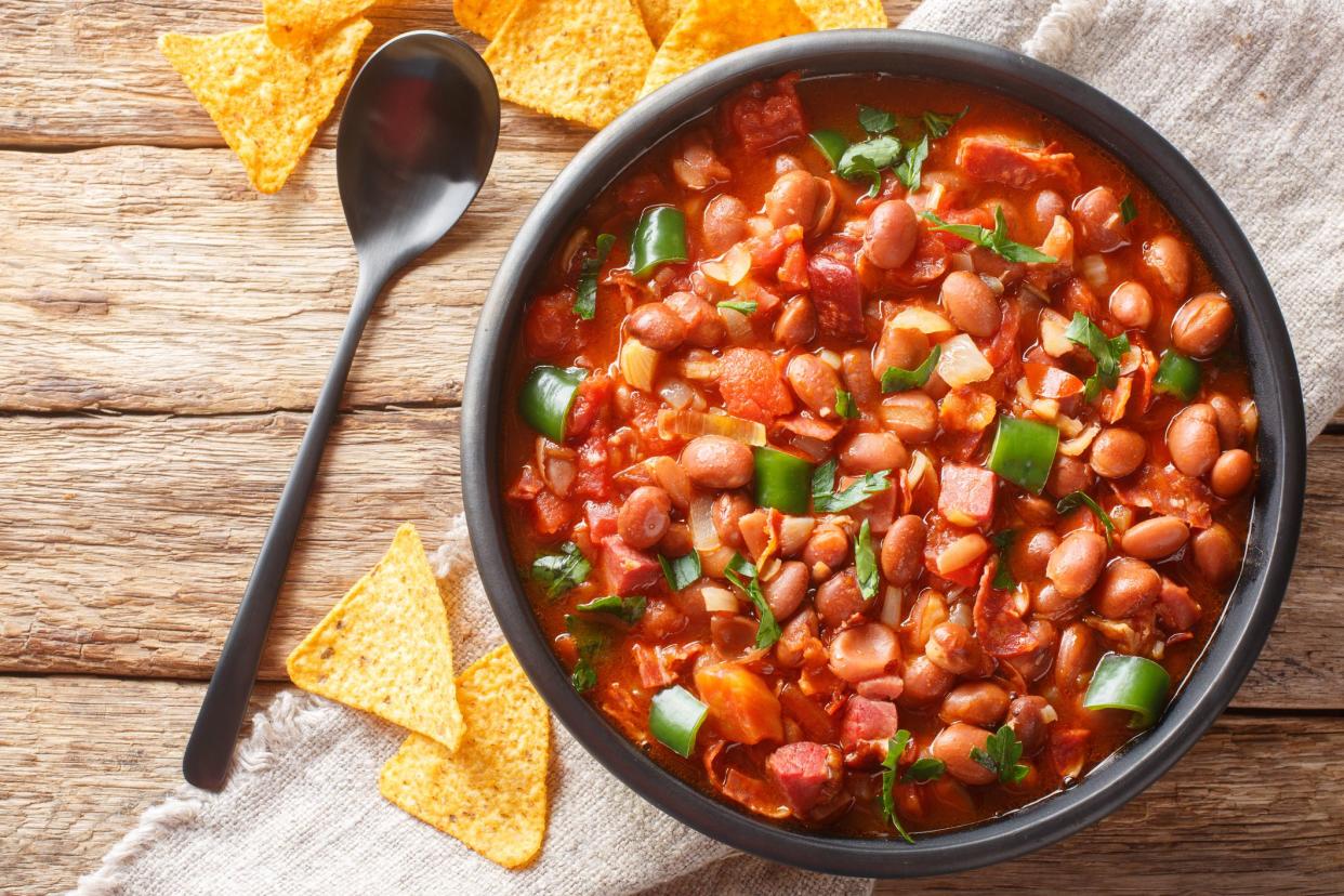 Mexican Charro Beans made with pinto beans, bacon, ham, chorizo, chili peppers, tomatoes and spices closeup on the bowl on the table. Horizontal top view from above