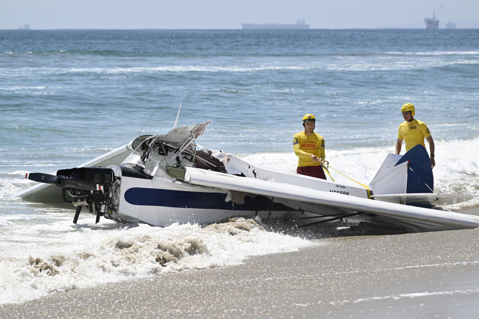 Investigators stand next to a small plane that was pulled from the water after it crashed into the ocean in Huntington Beach, Calif., Friday, July 22, 2022. The plane towing a banner crashed in the ocean Friday during a lifeguard competition that turned into a real-life rescue along the popular beach. (Brittany Murray/The Orange County Register via AP)