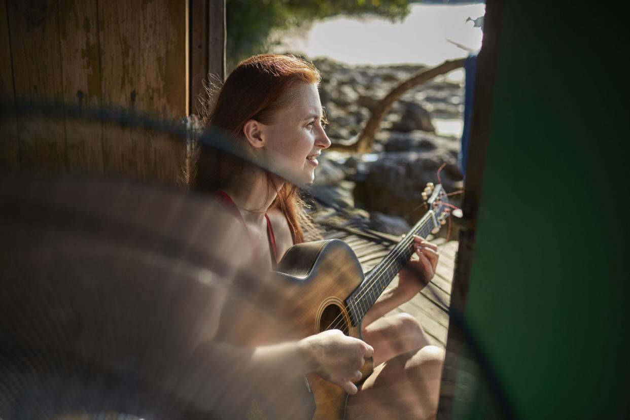 Young woman playing guitar in a hut at the sea with a fan in the foreground