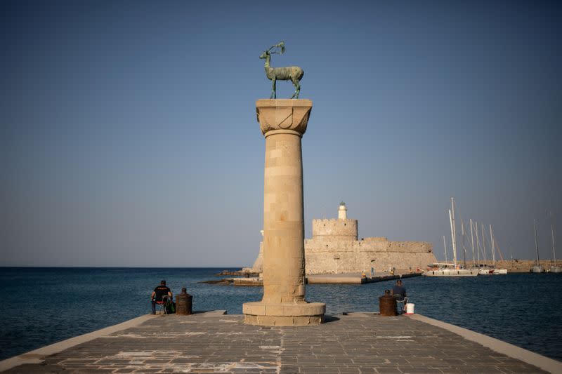 People fish next to the statue of a deer at the entrance of Mandraki harbour, following the coronavirus disease (COVID-19) outbreak, on the island of Rhodes